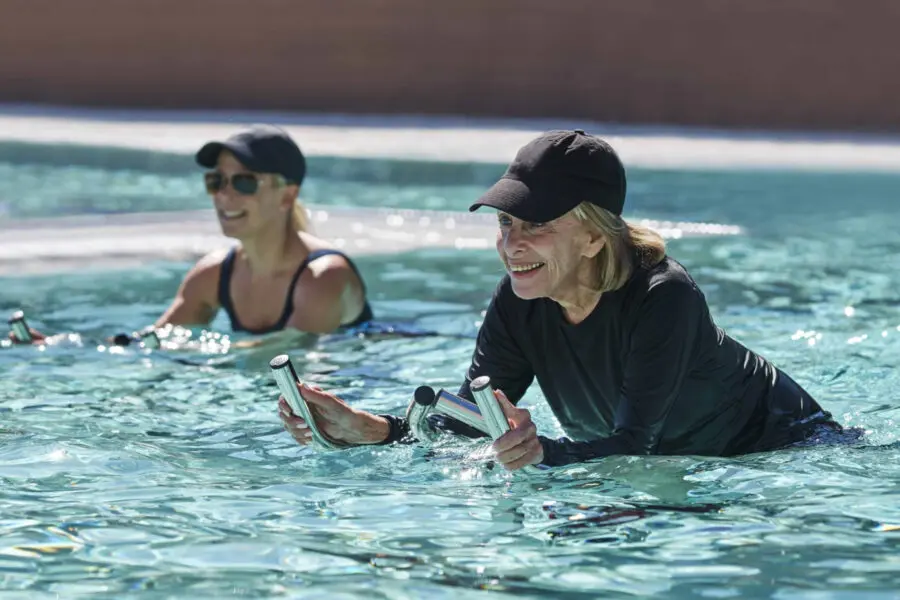 Two people exercise on aquatic exercise bikes in a bright blue pool.