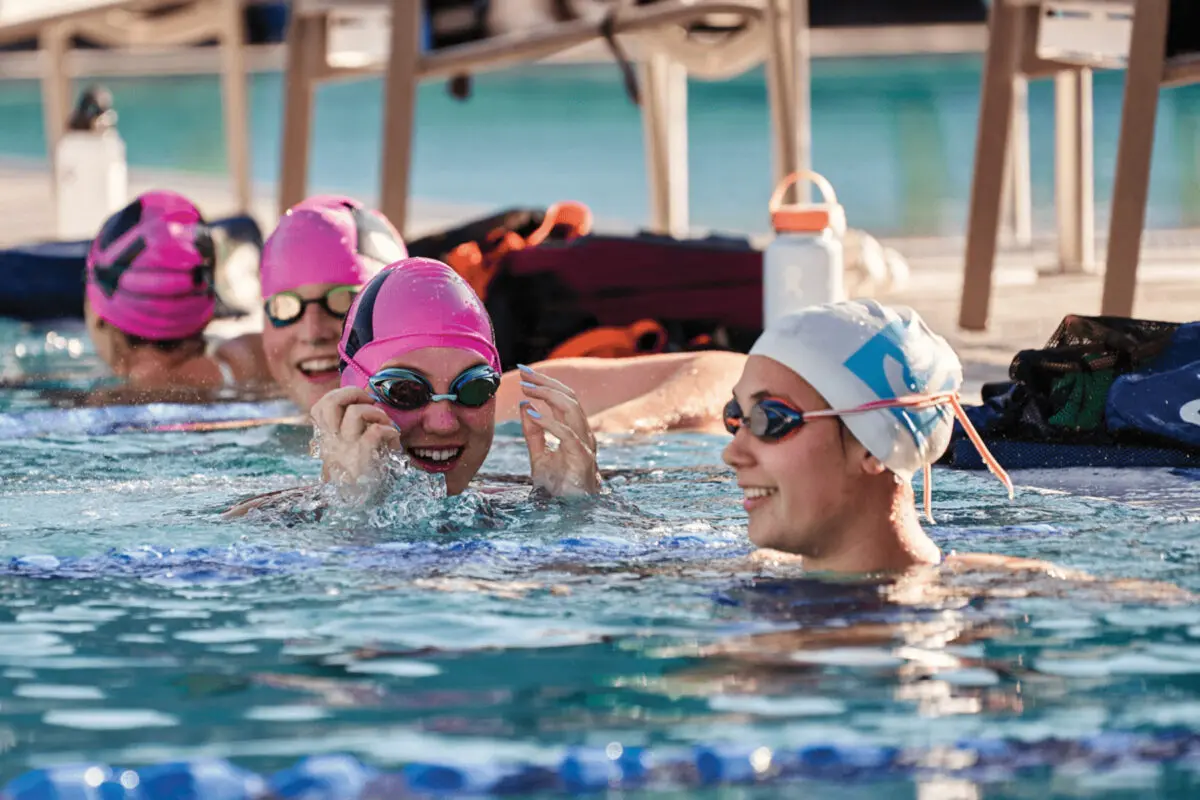 Members of the J Swim Team are in the pool, with pink caps and eye goggles.