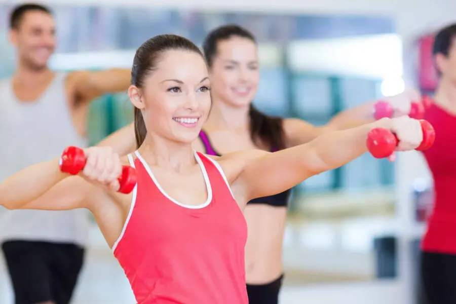 Several adults use weights and follow an instructor in a gym class.