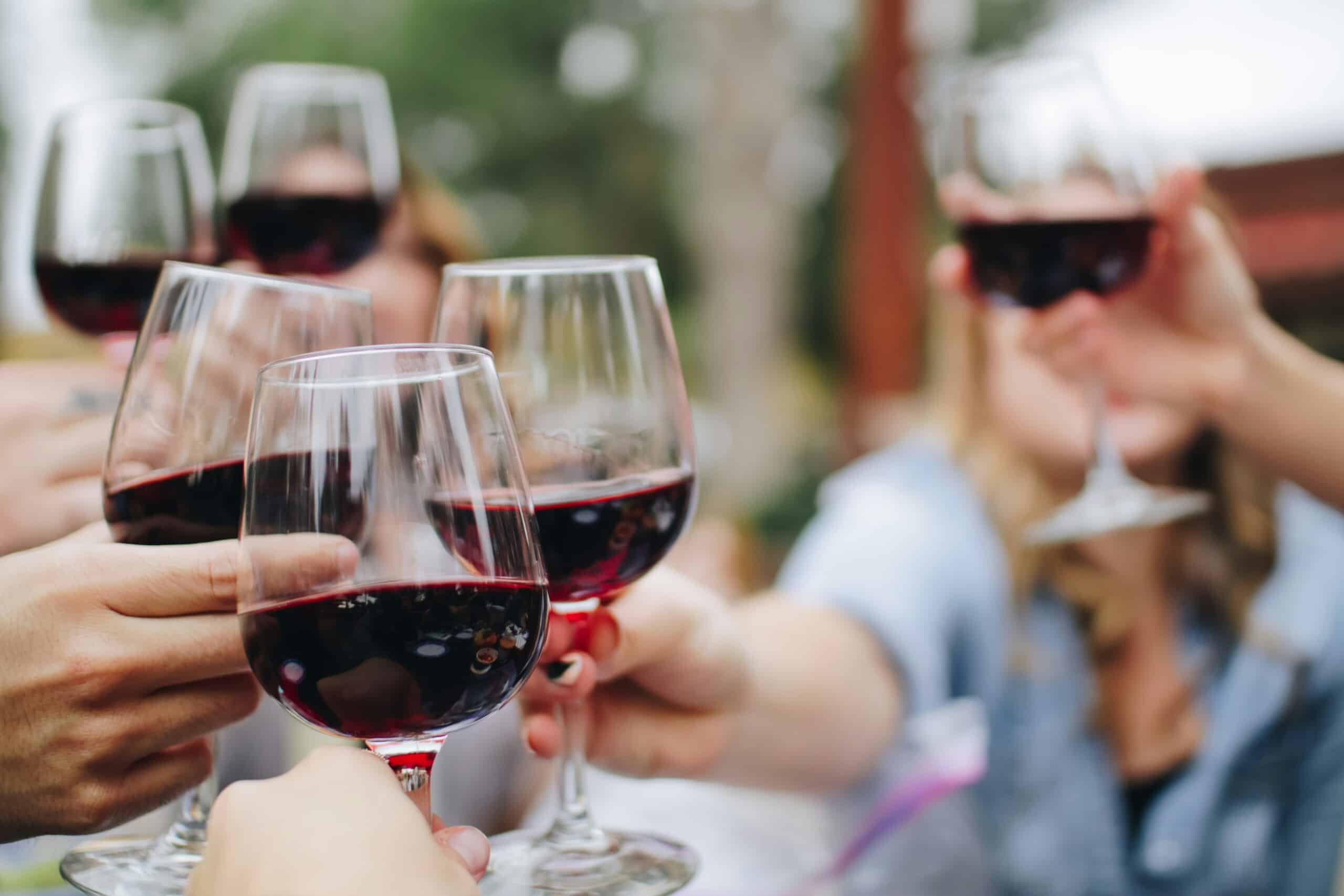 Several hands hold red wine in glasses and are bringing them together for a cheers.