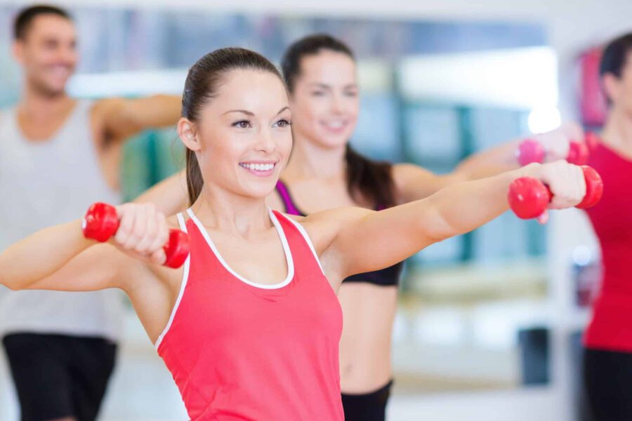 Several adults use weights and follow an instructor in a gym class.